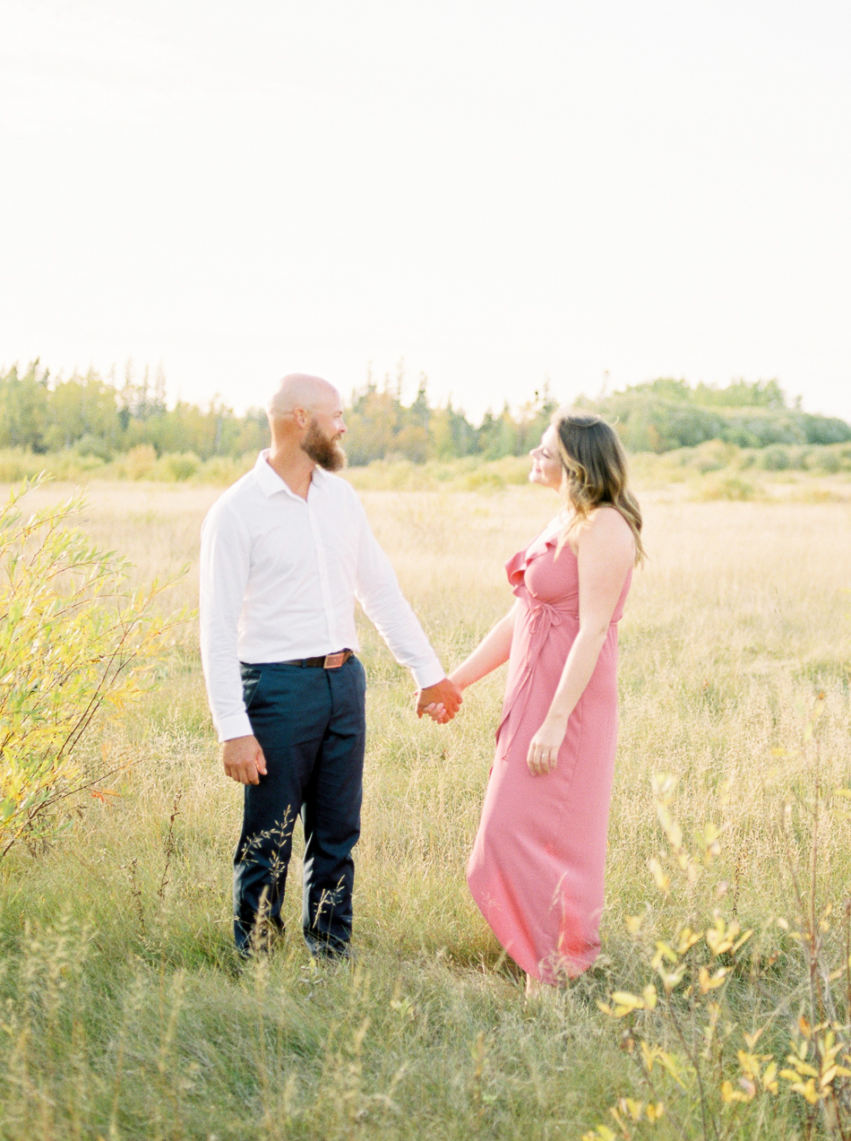 Fine Art Wedding Photographer Esther Funk Photography | A Semi Formal Birds Hill Provincial Park Engagement Session | A couple standing in a field | She is wearing a rose coloured dress