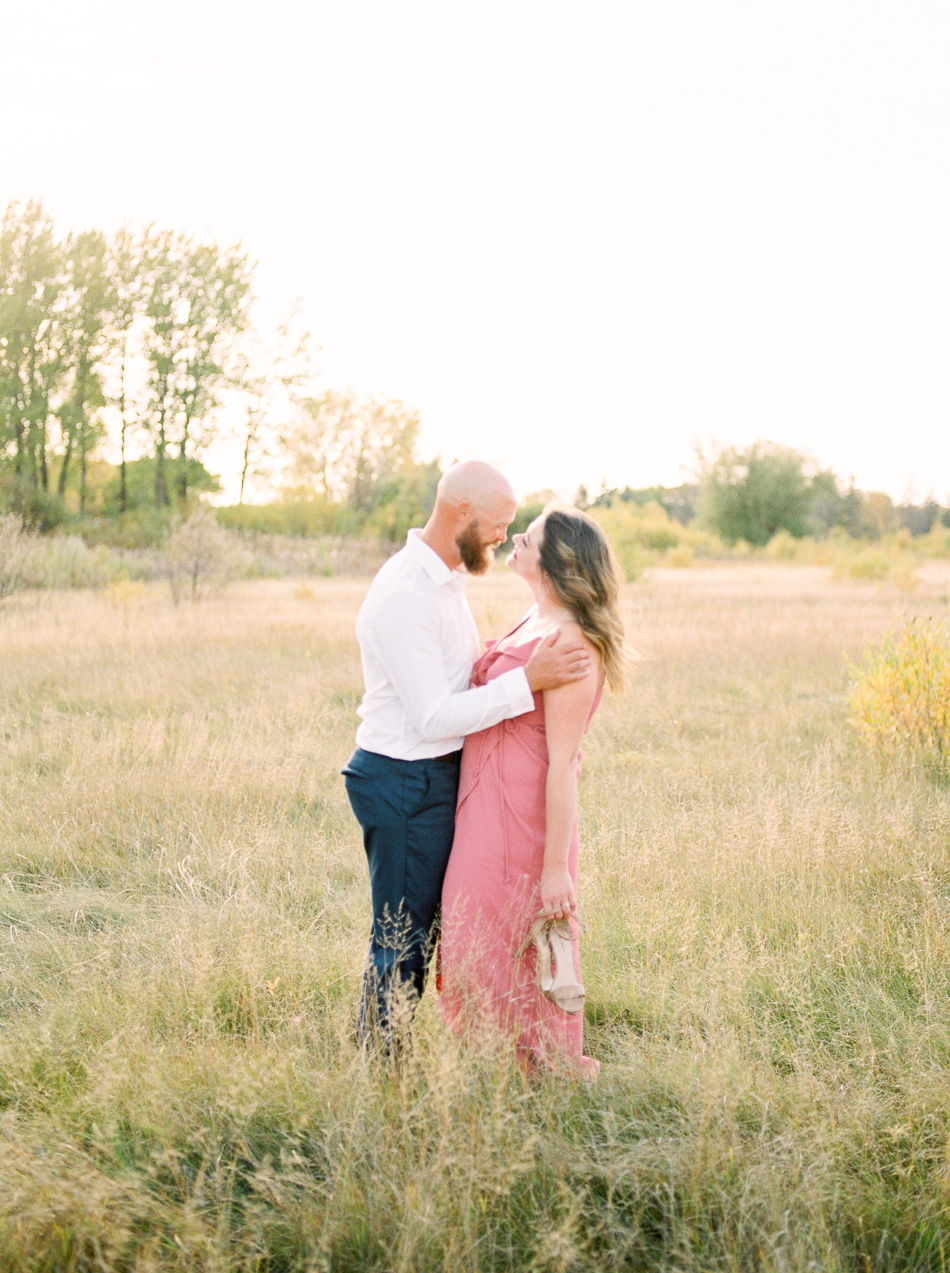 Fine Art Wedding Photographer Esther Funk Photography | A Semi Formal Birds Hill Provincial Park Engagement Session | A couple standing in a field gazing into each others eyes | She is wearing a rose coloured dress